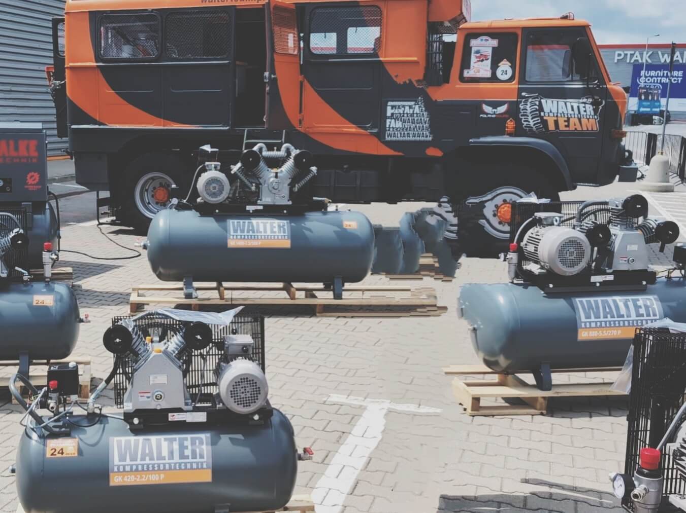 Ekspozycja profesjonalnych kompresorów tłokowych Walter na paletach przed pomarańczowym pojazdem serwisowym Walter Team w sklepie Anwa-Tech